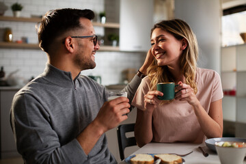 Happy girl enjoying in breakfast with her boyfriend. Loving young couple drinking coffee and eating sandwich at home...