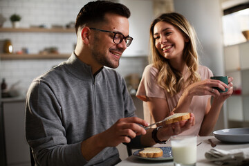 Happy girl enjoying in breakfast with her boyfriend. Loving young couple drinking coffee and eating sandwich at home...