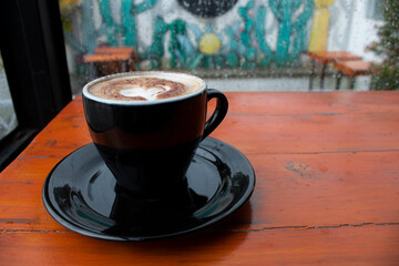 Warm coffee on a brown table and raindrops falling on the window