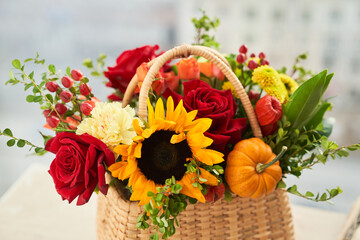 Mixed autumn flowers, sunflower, pumpkin, rose, physalis in basket, bouquet is on the windowsill. High quality photo