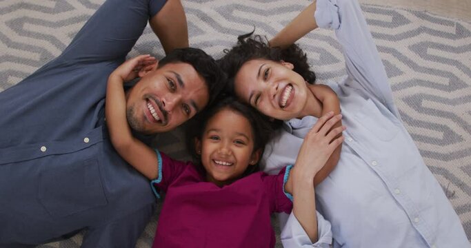 Happy hispanic parents and daughter embracing lying on floor in living room