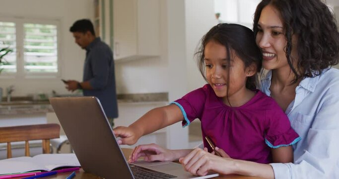 Happy hispanic mother and daughter sitting at table looking at laptop