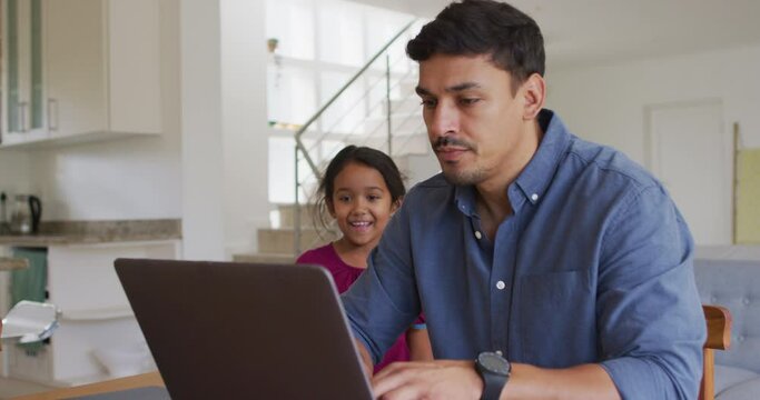 Happy hispanic father and daughter sitting at table looking at laptop