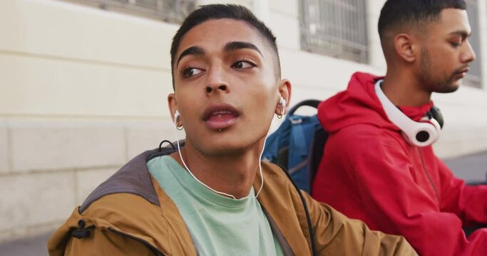 Two mixed race male friends wearing headphones, listening to music in the street