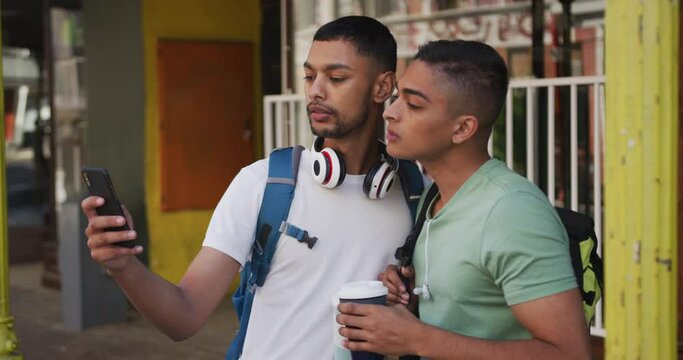 Two mixed race male friends drinking coffee and using smartphone in the street