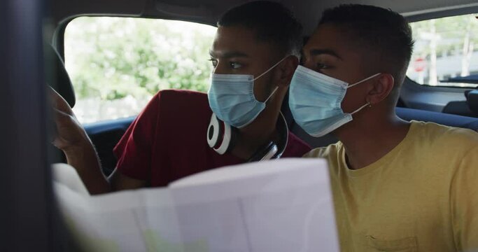 Two mixed race male friends wearing face masks using map in cab