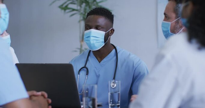 African american male doctor and diverse hospital colleagues wearing face masks talking at meeting