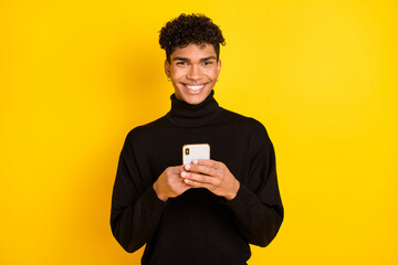 Photo of cute sweet dark skin guy dressed black turtleneck typing modern device isolated yellow color background