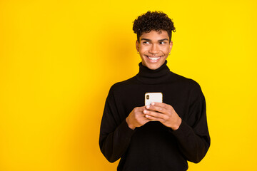 Photo of charming pretty dark skin man wear black jumper holding modern gadget looking empty space isolated yellow color background