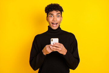 Photo of sweet impressed dark skin guy dressed turtleneck chatting device modern device isolated yellow color background