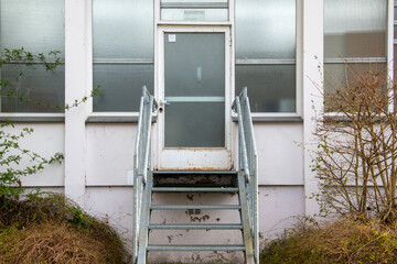 Metalltreppe zu einem alten, heruntergekommenen Gebäude mit einer angerosteten Tür.