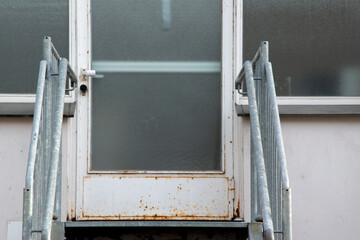 Metalltreppe zu einem alten, heruntergekommenen Gebäude mit einer angerosteten Tür.