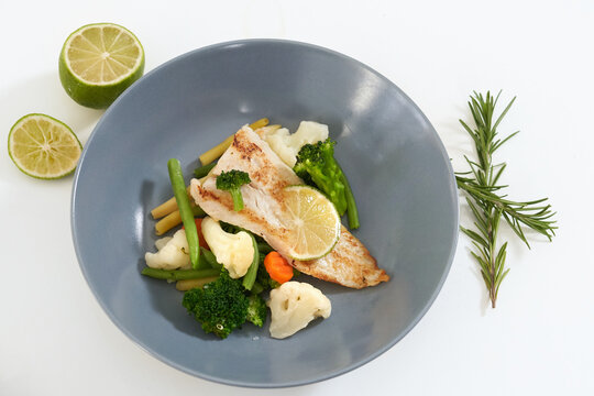 Close up of blue bowl with tasty steamed fish and vegetables with sprig of rosemary on white background. Concept of delicious food with good composition and for emaciation or support body. 