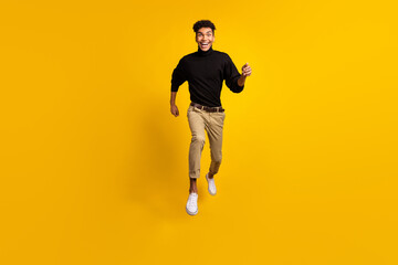 Fototapeta na wymiar Photo of attractive funny dark skin guy dressed black pullover jumping running fast isolated yellow color background