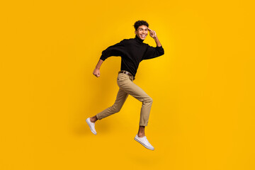 Fototapeta na wymiar Full size profile photo of optimistic nice brunet guy run look wear black sweater trousers sneakers isolated on yellow background