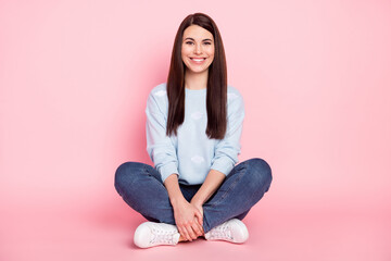 Full size photo of nice optimistic brunette hairdo lady sit wear shirt jeans sneakers isolated on pink color background