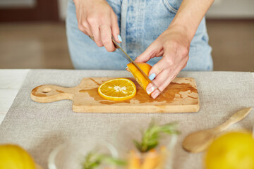 Female hand cut orange, Woman preparing, making citrus and rosemary fresh lemonade