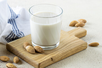 Non dairy almond milk in a glass on the wooden tray  on light rustic table close up.  Healthy vegan food concept.