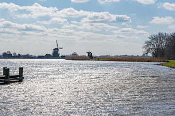 The sun shimmers in the choppy water of the lake De Rottemeren near windmill De Korenmolen on a sunny and windy day