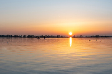 Two persons on paddleboards paddle their way home during a sunset at lake Zoetermeerse Plas, the Netherlands