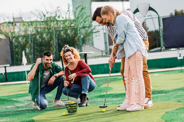 Fototapeta premium Group of smiling friends enjoying together playing mini golf in the city.