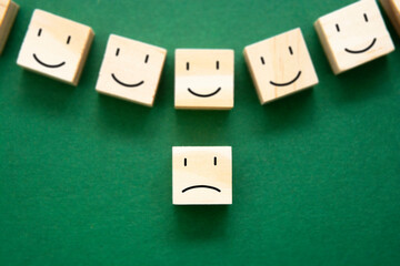 Sad smile against happy smiles on wooden blocks over green background. Depression, mental health.