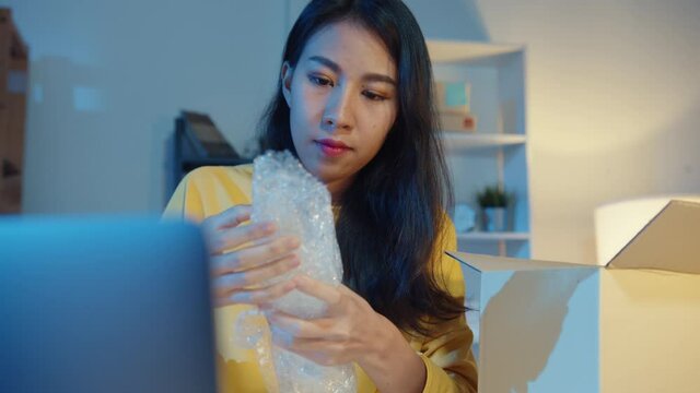 Young Asia businesswoman packing glass use bubble wrap for packing support damage fragile product in home office at night. Small business owner, online market delivery, lifestyle freelance concept.