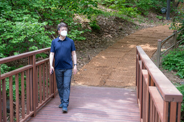 Middle-aged Asian man walking alone in a forest path wearing a face mask.