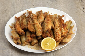 Small fried fish with breadcrumbs on a white plate with fresh lemon. Fried small fish in breading, close-up on a plate. horizontal view from above 