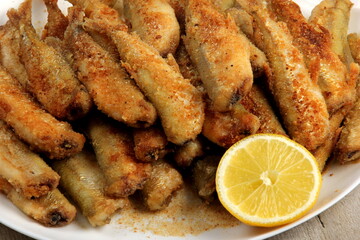 Small fried fish with breadcrumbs on a white plate with fresh lemon. Fried small fish in breading, close-up on a plate. horizontal view from above 