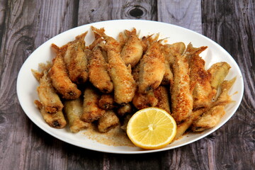 Small fried fish with breadcrumbs on a white plate with fresh lemon. Fried small fish in breading, close-up on a plate. horizontal view from above 