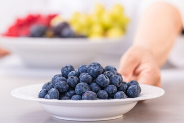 Dish of blueberries with a women's hand out of focus: close up and selective focus.