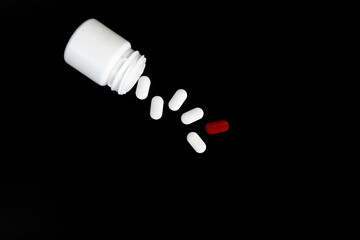 A white jar with scattered pills on a black background. High quality photo