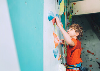 Smiling teenager boy at indoor climbing wall hall. The boy is climbing using a top rope and climbing harness. Active teenager time spending concept image