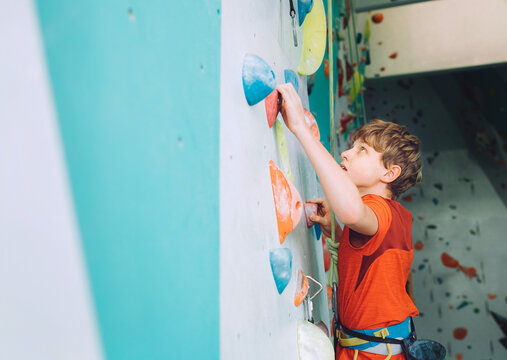 Smiling teenager boy at indoor climbing wall hall. The boy is climbing using a top rope and climbing harness. Active teenager time spending concept image