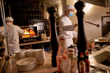 Cook holding ladle above a frying pan in kitchen