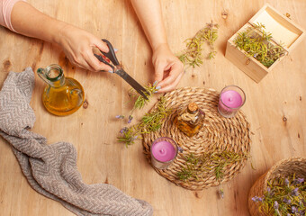 Vista de las manos de una mujer cortando ramas de flor de lavanda para hacer aceite de lavanda en una mesa de madera con dos velas aromáticas de lavanda  y ramas de flor de lavanda en una caja.