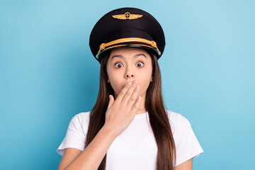 Portrait of attractive amazed girl captain wearing hat closing mouth oops isolated over bright blue...