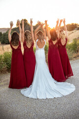 bridesmaids in red dress and bride on her back with raised hands looking at the sunset together. bridesmaids concept