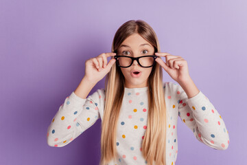 Photo of impressed clever geek nerd kid girl touch specs on violet background