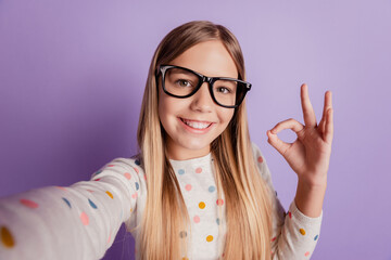 Lovely cute kid girl make selfie ok symbol advertise isolated over purple background