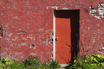 Red brick stone wall, with red door. Weatheredfacade.