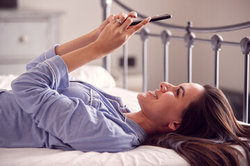 Obraz na płótnie Canvas Woman Wearing Pyjamas Taking Selfie On Mobile Phone Lying On Bed