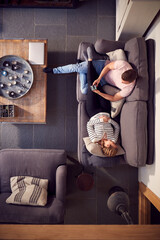 Overhead View Of Couple Relaxing On Lounge Sofa At Home And Using Mobile Phone