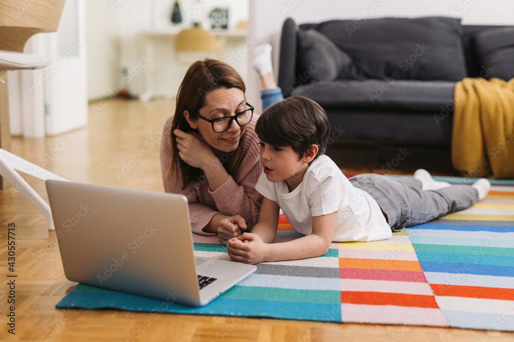 Wall mural mother and son laying on floor in living room and using laptop computer