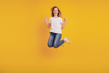 Fototapeta na wymiar Smiling positive girl jumping on yellow background raise fists celebrate victory