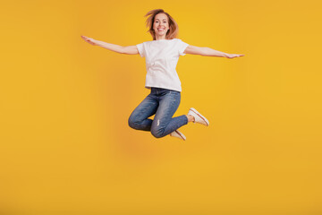 Fototapeta na wymiar Smiling positive girl jumping hands wings inspiration on yellow background