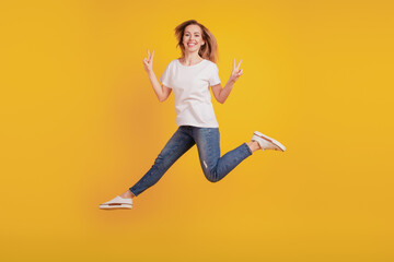 Smiling positive girl jumping run show v-sign on yellow background