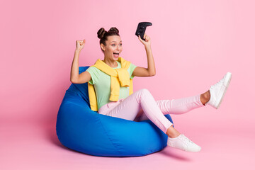 Photo of lucky shiny young lady dressed green t-shirt sitting bean bag play station looking empty space isolated pink color background