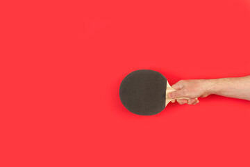 Mano de hombre sosteniendo una raqueta de ping pong  sobre un fondo rojo liso y aislado. Vista de...